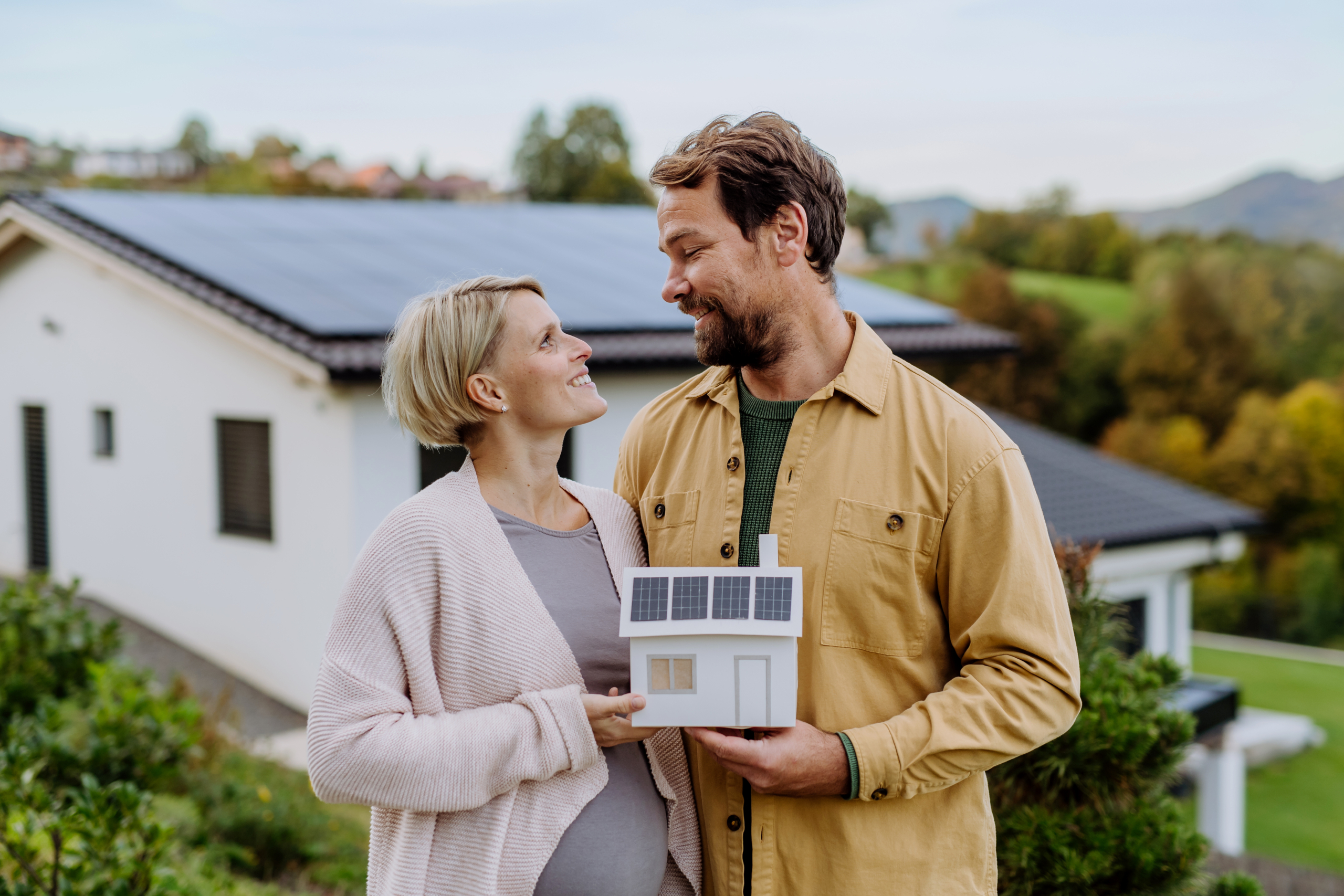 Close up of happy couple holding paper model of house with solar panels. Alternative energy, saving resources and sustainable lifestyle concept.